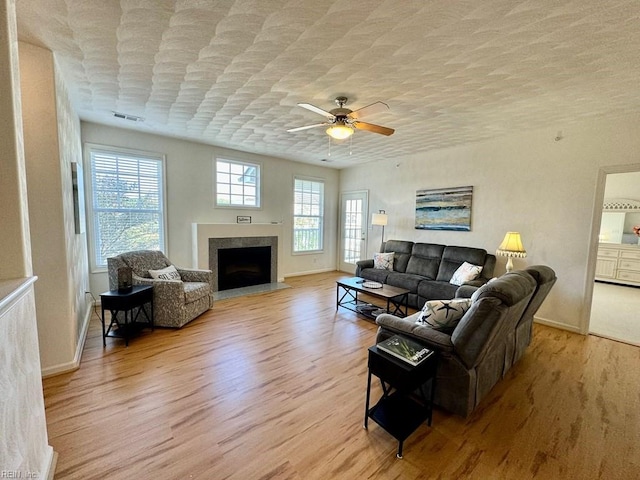 living room featuring ceiling fan, a textured ceiling, a fireplace, and light hardwood / wood-style flooring