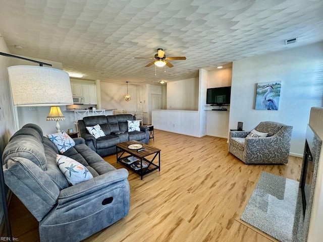 living room featuring ceiling fan, a textured ceiling, and light wood-type flooring