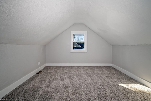 additional living space with lofted ceiling, carpet floors, and a textured ceiling