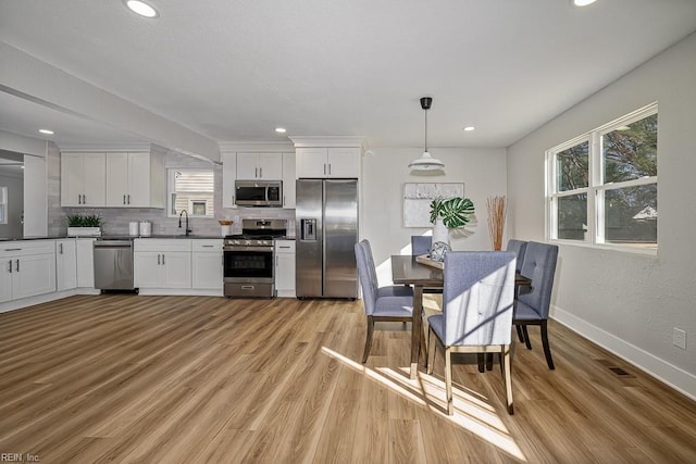 kitchen featuring white cabinetry, pendant lighting, stainless steel appliances, light hardwood / wood-style floors, and backsplash