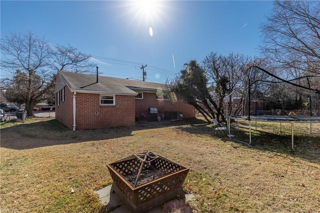 view of side of home featuring a yard, a trampoline, and an outdoor fire pit