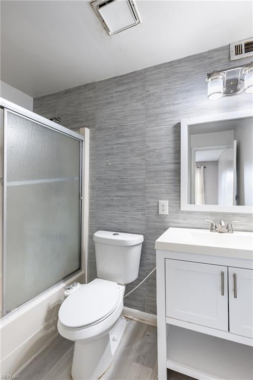 full bathroom with toilet, combined bath / shower with glass door, tile walls, vanity, and hardwood / wood-style floors