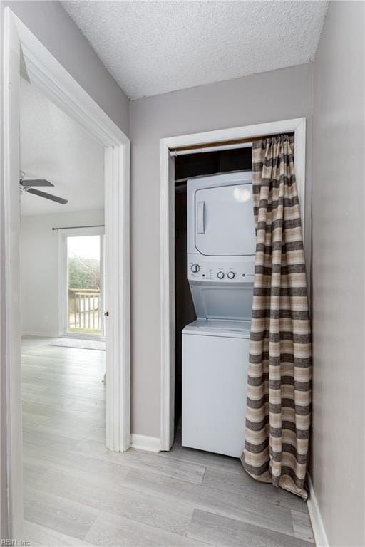 laundry area with ceiling fan, stacked washer and clothes dryer, light hardwood / wood-style floors, and a textured ceiling