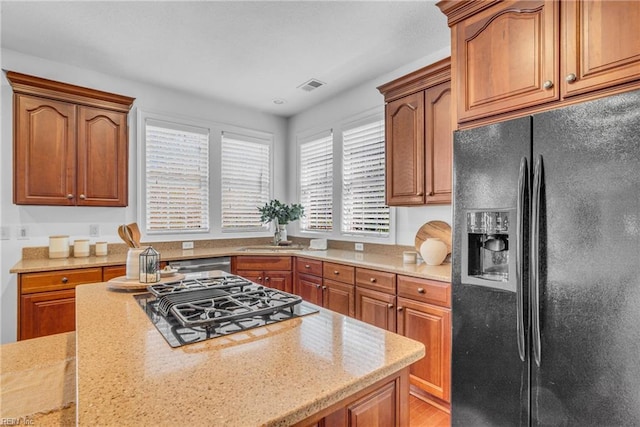 kitchen featuring brown cabinetry, visible vents, stainless steel gas stovetop, and black fridge