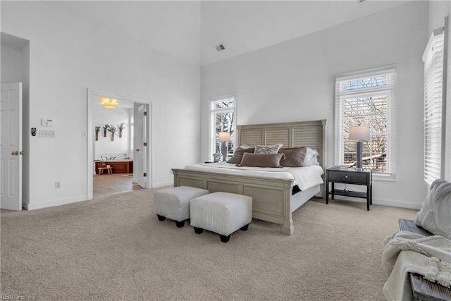 bedroom featuring baseboards, light carpet, a high ceiling, and ensuite bathroom