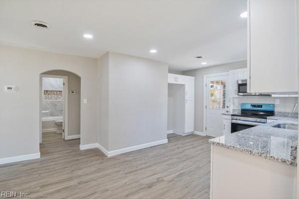 kitchen with sink, light stone counters, light wood-type flooring, appliances with stainless steel finishes, and white cabinets