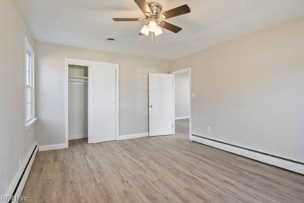 unfurnished bedroom featuring a baseboard radiator, ceiling fan, light wood-type flooring, and a closet