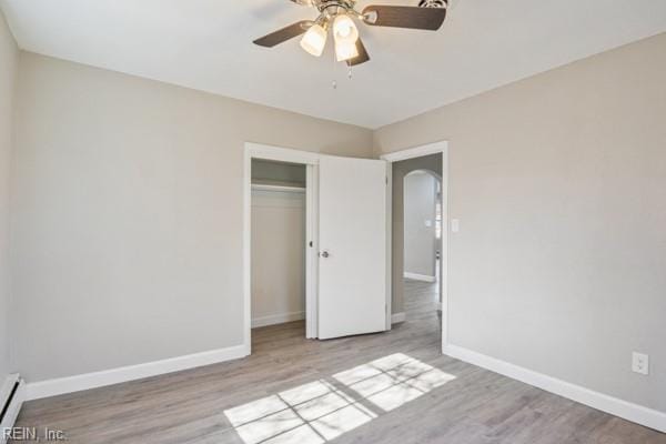 unfurnished bedroom featuring a baseboard radiator, a closet, ceiling fan, and light wood-type flooring