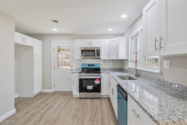 kitchen with white cabinetry, sink, light stone counters, stainless steel appliances, and plenty of natural light