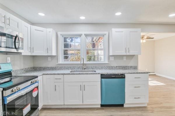 kitchen with sink, appliances with stainless steel finishes, white cabinetry, light stone counters, and light hardwood / wood-style floors