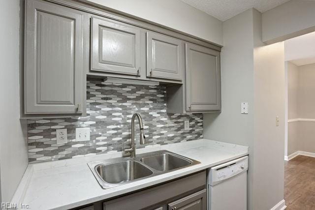 kitchen with wood-type flooring, sink, gray cabinetry, backsplash, and white dishwasher