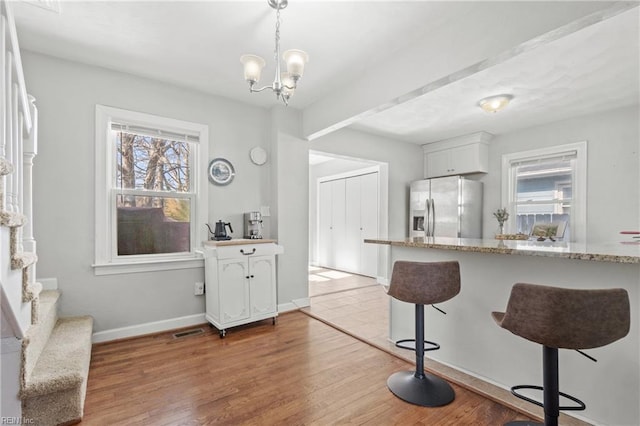 kitchen with a breakfast bar, pendant lighting, white cabinetry, stainless steel refrigerator with ice dispenser, and light stone countertops