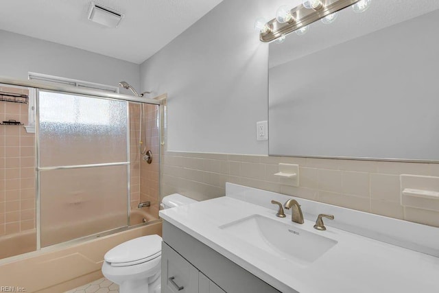 full bathroom featuring combined bath / shower with glass door, tile walls, vanity, tile patterned floors, and toilet