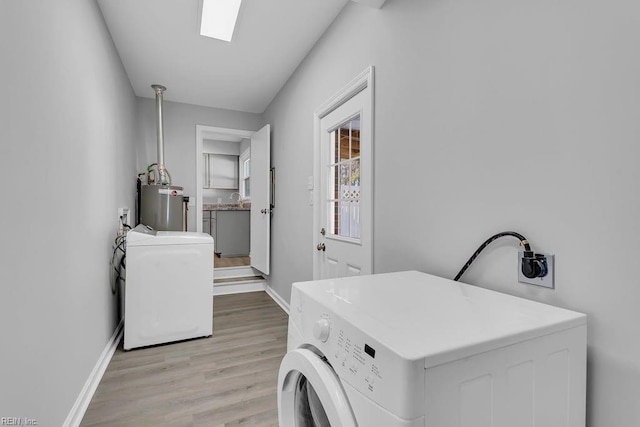 clothes washing area featuring sink, a skylight, independent washer and dryer, gas water heater, and light wood-type flooring