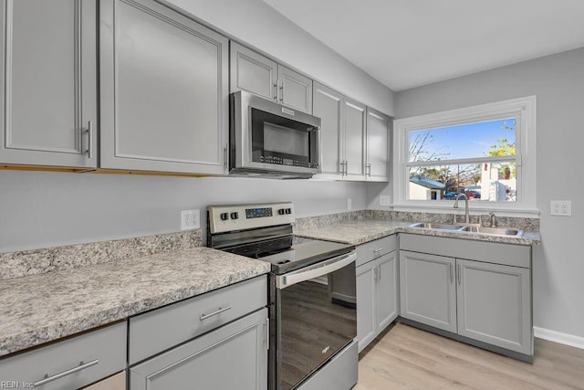 kitchen with stainless steel appliances, light hardwood / wood-style floors, sink, and gray cabinetry