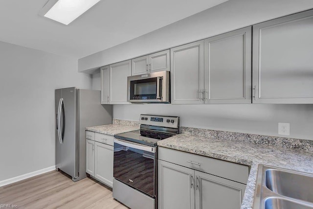 kitchen with gray cabinetry, sink, stainless steel appliances, and light hardwood / wood-style floors