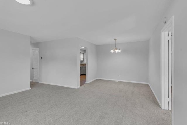 spare room featuring light colored carpet and an inviting chandelier