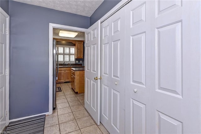 corridor with sink, a textured ceiling, and light tile patterned floors