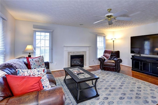 living room featuring wood-type flooring, a high end fireplace, ceiling fan, and a textured ceiling