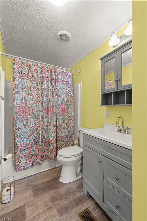 full bathroom with shower / tub combo with curtain, vanity, wood-type flooring, a textured ceiling, and toilet