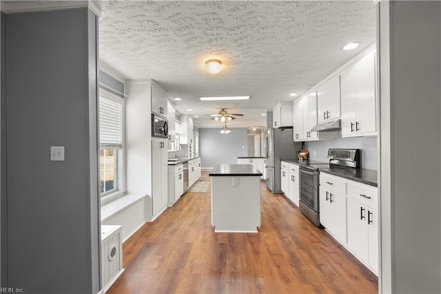 kitchen featuring appliances with stainless steel finishes, white cabinets, dark hardwood / wood-style flooring, a center island, and ceiling fan