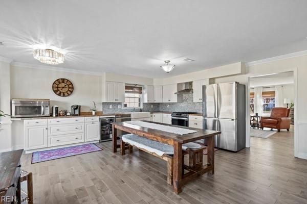 kitchen with backsplash, stainless steel appliances, white cabinets, beverage cooler, and wall chimney exhaust hood