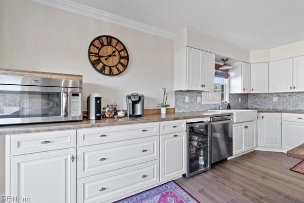 kitchen with appliances with stainless steel finishes, white cabinetry, beverage cooler, backsplash, and ornamental molding