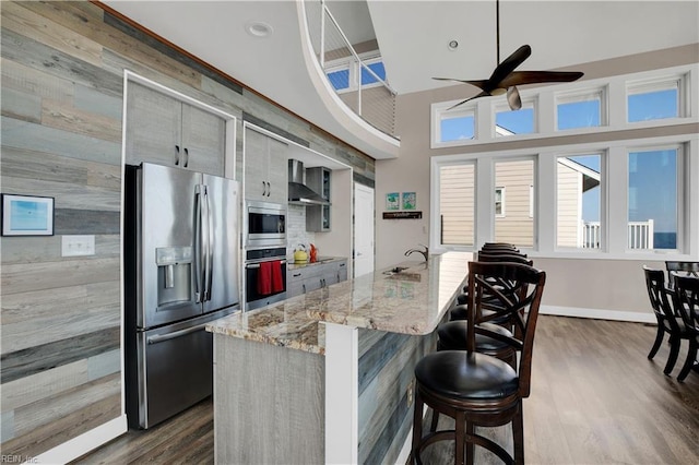 kitchen with appliances with stainless steel finishes, dark hardwood / wood-style floors, a kitchen bar, and wall chimney exhaust hood