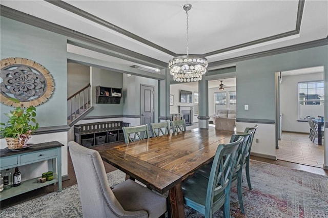 dining room with ornamental molding, a raised ceiling, ceiling fan with notable chandelier, and wood-type flooring