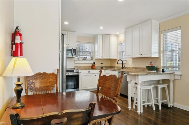 kitchen with stainless steel appliances, a kitchen breakfast bar, light stone countertops, white cabinets, and dark hardwood / wood-style flooring