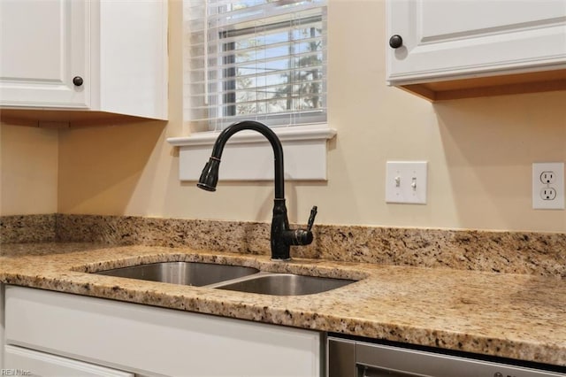 interior details featuring white cabinetry, stainless steel dishwasher, light stone countertops, and sink