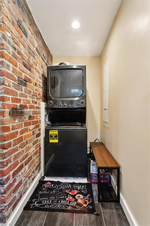 interior space with stacked washer / drying machine, dark hardwood / wood-style floors, and brick wall