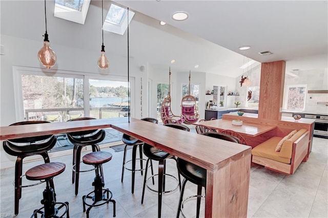 kitchen with a breakfast bar area, hanging light fixtures, lofted ceiling with skylight, a center island, and oven