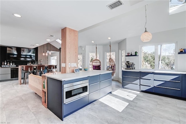 kitchen featuring blue cabinets, a kitchen island, stainless steel microwave, and decorative light fixtures