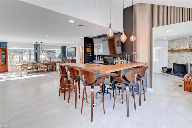 kitchen featuring butcher block counters, a brick fireplace, a kitchen breakfast bar, pendant lighting, and a high ceiling