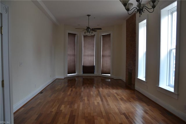 empty room with dark wood-type flooring and ceiling fan with notable chandelier