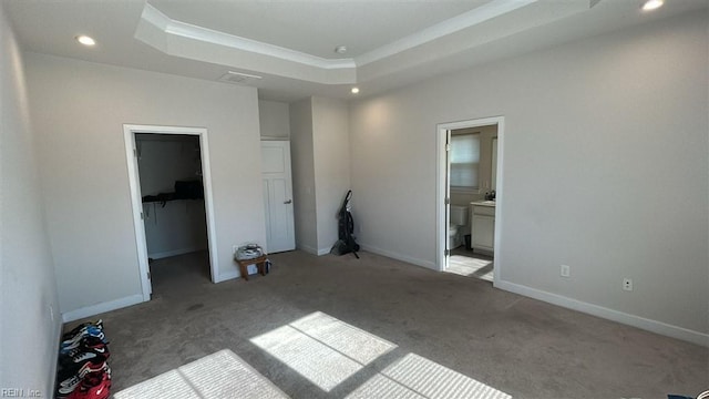 unfurnished bedroom featuring a walk in closet, a tray ceiling, light colored carpet, and ensuite bath