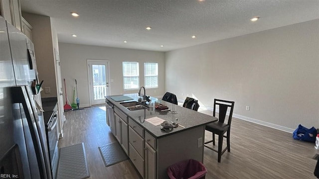 kitchen featuring sink, refrigerator, a kitchen island with sink, gray cabinetry, and a kitchen breakfast bar