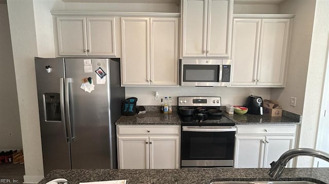 kitchen with stainless steel appliances, white cabinetry, sink, and dark stone countertops