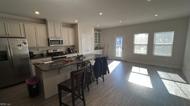 kitchen featuring dark wood-type flooring, a center island with sink, a textured ceiling, appliances with stainless steel finishes, and a kitchen breakfast bar