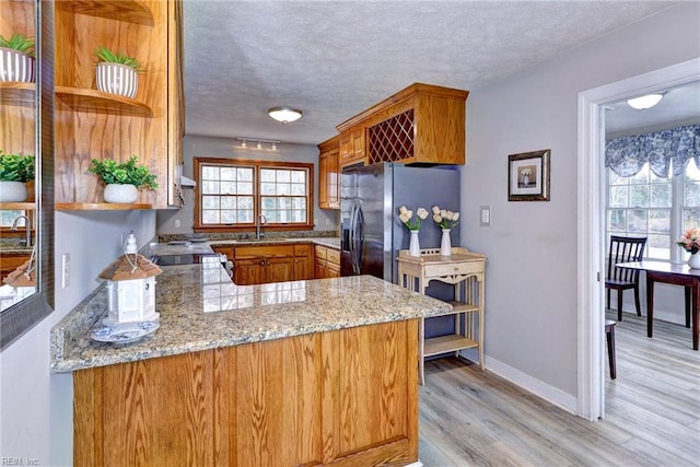 kitchen with sink, light stone counters, a textured ceiling, stainless steel fridge with ice dispenser, and kitchen peninsula