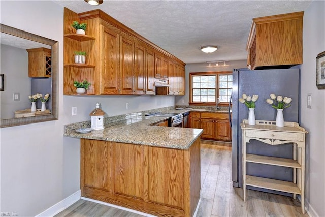 kitchen with appliances with stainless steel finishes, light stone counters, kitchen peninsula, a textured ceiling, and light hardwood / wood-style flooring