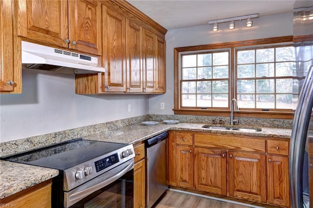 kitchen with appliances with stainless steel finishes, light stone countertops, sink, and light wood-type flooring