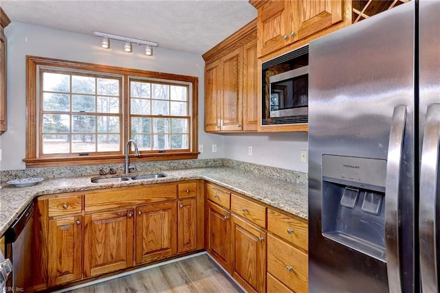 kitchen featuring sink, stainless steel appliances, light hardwood / wood-style floors, and light stone countertops