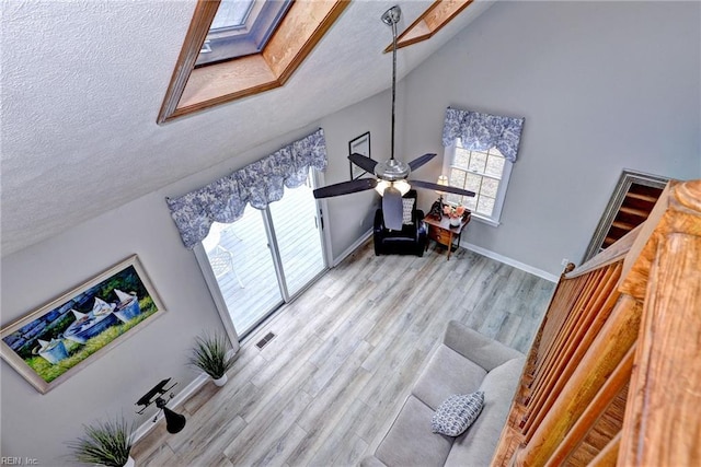 living room featuring vaulted ceiling, ceiling fan, a textured ceiling, and light hardwood / wood-style floors