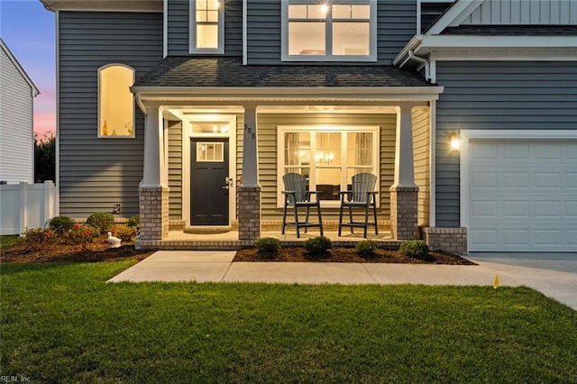 exterior entry at dusk featuring a garage, a yard, and covered porch