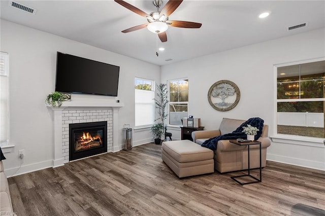 living area with a brick fireplace, hardwood / wood-style floors, and ceiling fan