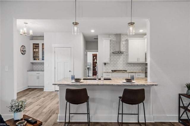 kitchen with white cabinetry, wall chimney exhaust hood, decorative light fixtures, and light stone countertops