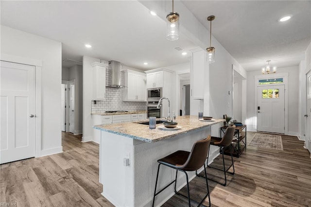 kitchen with appliances with stainless steel finishes, decorative light fixtures, white cabinetry, sink, and wall chimney range hood