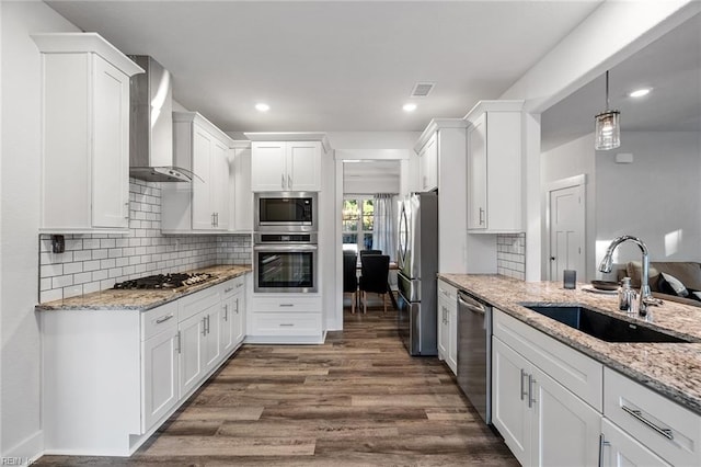 kitchen with pendant lighting, white cabinetry, sink, stainless steel appliances, and wall chimney exhaust hood